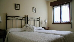 Una cama doble con cabecera, dos mesitas de noche, una ventana con cortinas y dos cuadros enmarcados en la pared.
