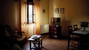 Una sala de estar con sofá, una mesa con libros, televisor y un comedor con sillas y un florero.