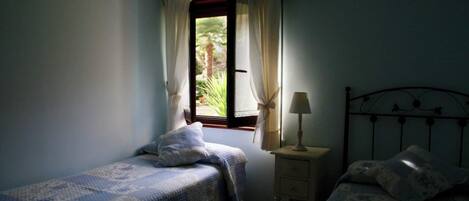 Een slaapkamer met twee eenpersoonsbedden, een nachtkastje met een lamp en een raam met gordijnen.