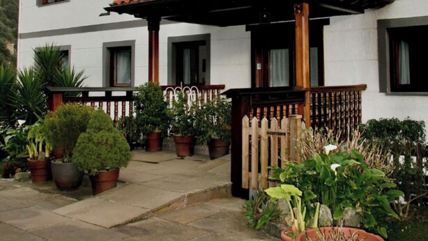 A two-story building with a white facade, multiple windows, and a wooden balcony. - Apartment 2 (Peñamellera Baja)
