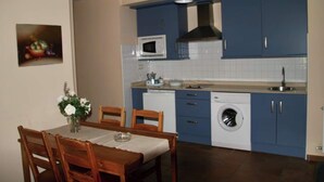 A compact kitchen with blue cabinets, a microwave, a dishwasher, and a dining area with a table and chairs. - Apartment 2 (Peñamellera Baja)