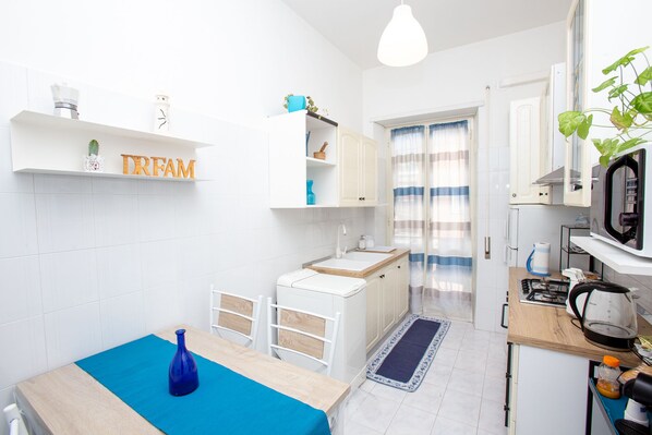 Une cuisine compacte avec des meubles blancs, un évier, une cuisinière et un four à micro-ondes. Il y a un petit coin repas avec une table et des chaises.