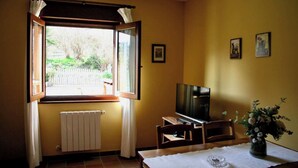 Ein Zimmer mit Fernseher auf einem Holzständer, einem Esstisch mit Blumenvase und einem Fenster mit Vorhängen.
