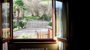 Ein Zimmer mit großem Fenster, das auf einen Garten mit Holzzaun, einer Bank und verschiedenen Pflanzen blickt.