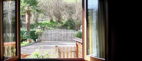 A room with a large window overlooking a garden with a wooden fence, a bench, and various plants.