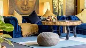 Un sofá azul con una mesa redonda de madera al frente, un cuadro de Buda en la pared y un frutero sobre la mesa.