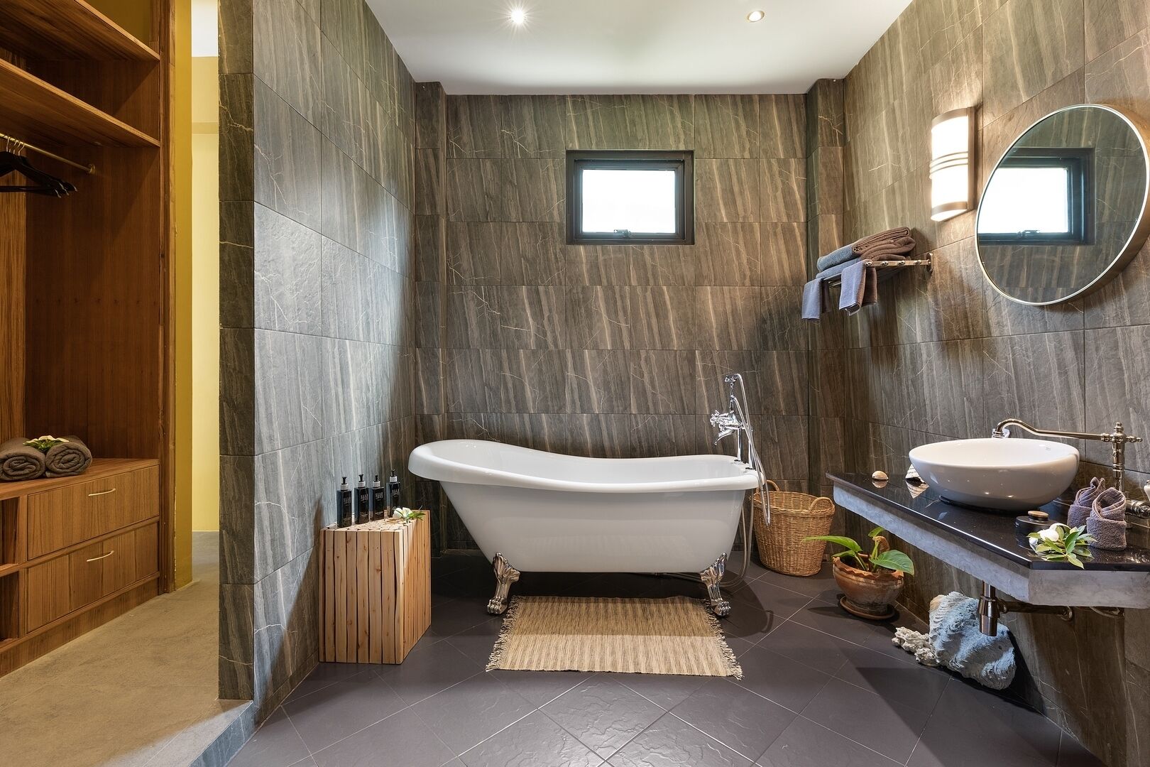 Une salle de bain moderne avec une baignoire sur pieds, un meuble-lavabo et un meuble en bois où sont rangées les serviettes.