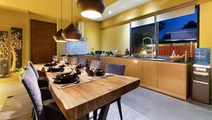 Un comedor moderno con una mesa de madera dispuesta para una comida, una cocina al fondo y un ventanal con vistas al exterior.