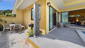 Un patio exterior moderno con zona de estar, una parrilla y un box de ducha con mosaicos.