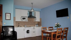 A compact kitchen with white cabinets, a microwave, a washing machine, and a dining area with a wooden table and chairs. - Apartment 5 (Peñamellera Baja)