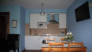 A compact kitchen with white cabinets, a microwave, a stove, and a sink. There is a dining table with chairs and a vase with flowers. - Apartment 5 (Peñamellera Baja)