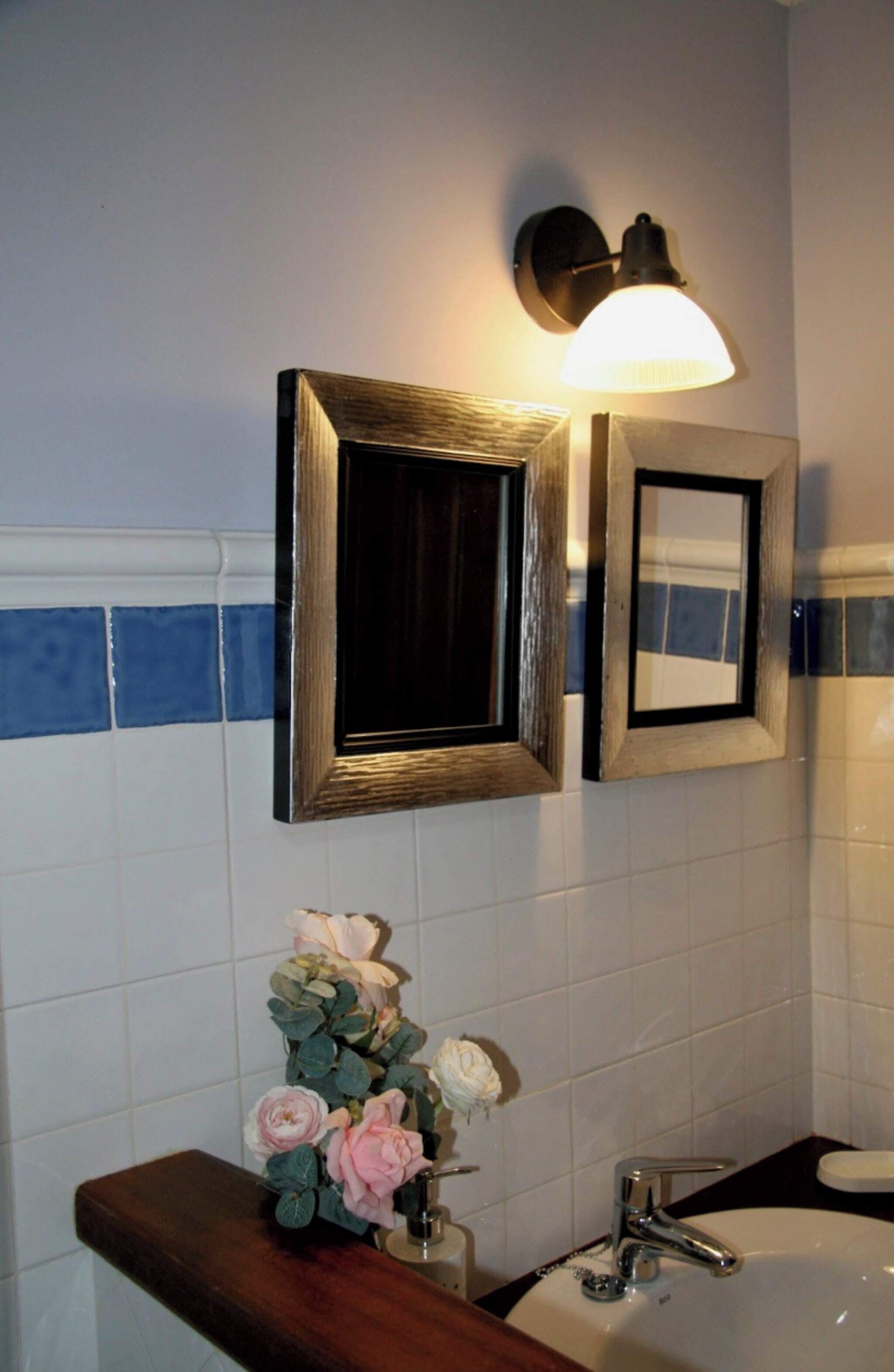 A bathroom with a sink, a mirror, and a wall-mounted light fixture.
