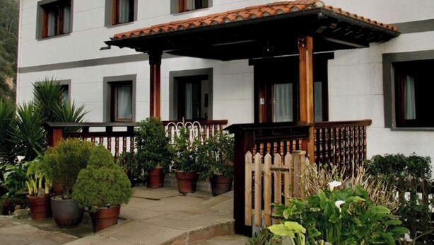 A two-story building with a white facade, multiple windows, and a wooden balcony. - Apartment 5 (Peñamellera Baja)