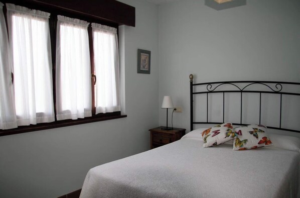 A bedroom with a bed, a nightstand, a lamp, and a window with curtains.