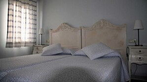 A neatly made bed with a patterned bedspread, two pillows, and a headboard with decorative carvings. There are two bedside tables with lamps, and a window with curtains. - Apartment 5 (Peñamellera Baja)