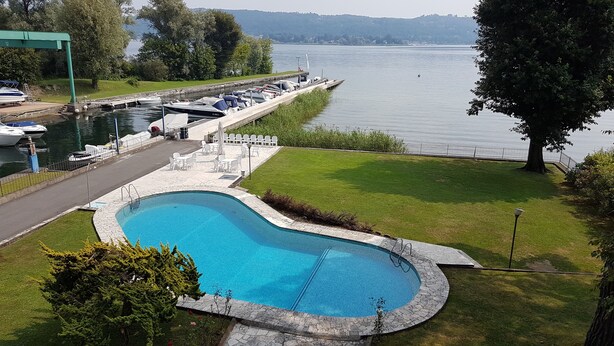 A swimming pool with a stone border, surrounded by a grassy area and a dock with boats. - EVASION AU FIL DE L'EAU.... (CIN IT003062C24G5JPZGD) (DORMELLETTO)