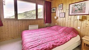 Un dormitorio con una cama grande, paredes de madera y vistas a un paisaje montañoso a través de dos ventanas.