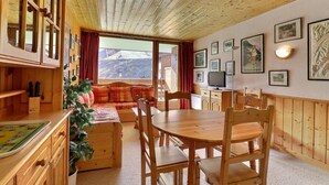 Un interior de madera acogedor con zona de comedor, cocina y un amplio ventanal con vistas a la montaña.