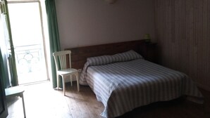 A bedroom with a wooden floor, a bed with a striped bedspread, a chair, and a ceiling light fixture.