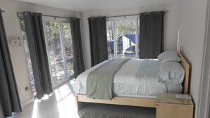 Ein Schlafzimmer mit Bett, Nachttisch, Teppich und Blick ins Freie.