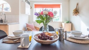 Disposição para o café da manhã com uma tigela de uvas e croissants, um vaso de flores e uma xícara de café sobre uma mesa.