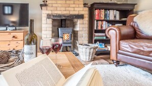 Uma sala de estar acolhedora com lareira, um sofá de couro, uma estante de livros e uma mesa com uma garrafa de vinho e copos.
