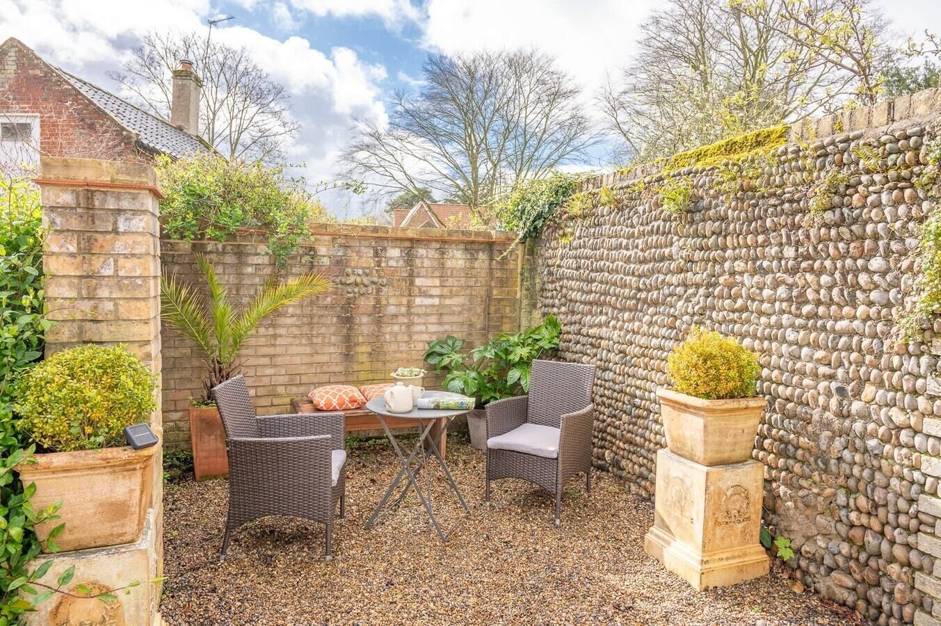 A patio area with wicker furniture, a stone wall, and potted plants.