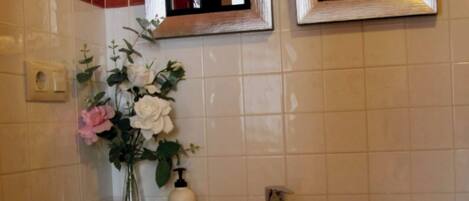 Un baño con un lavamanos blanco, dos espejos enmarcados, un florero con flores y un perchero para toallas.