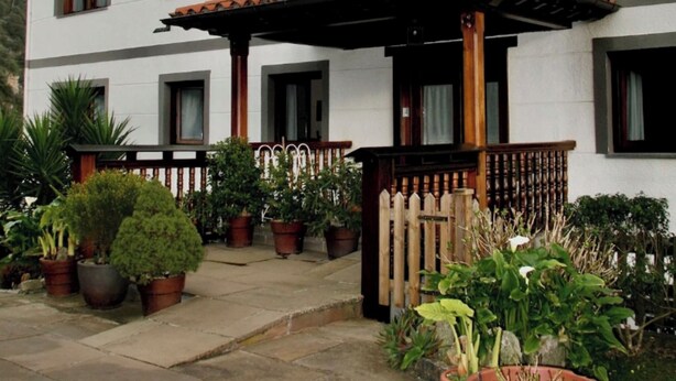 Un edifici de dues plantes amb façana blanca, nombroses finestres i un balcó de fusta.