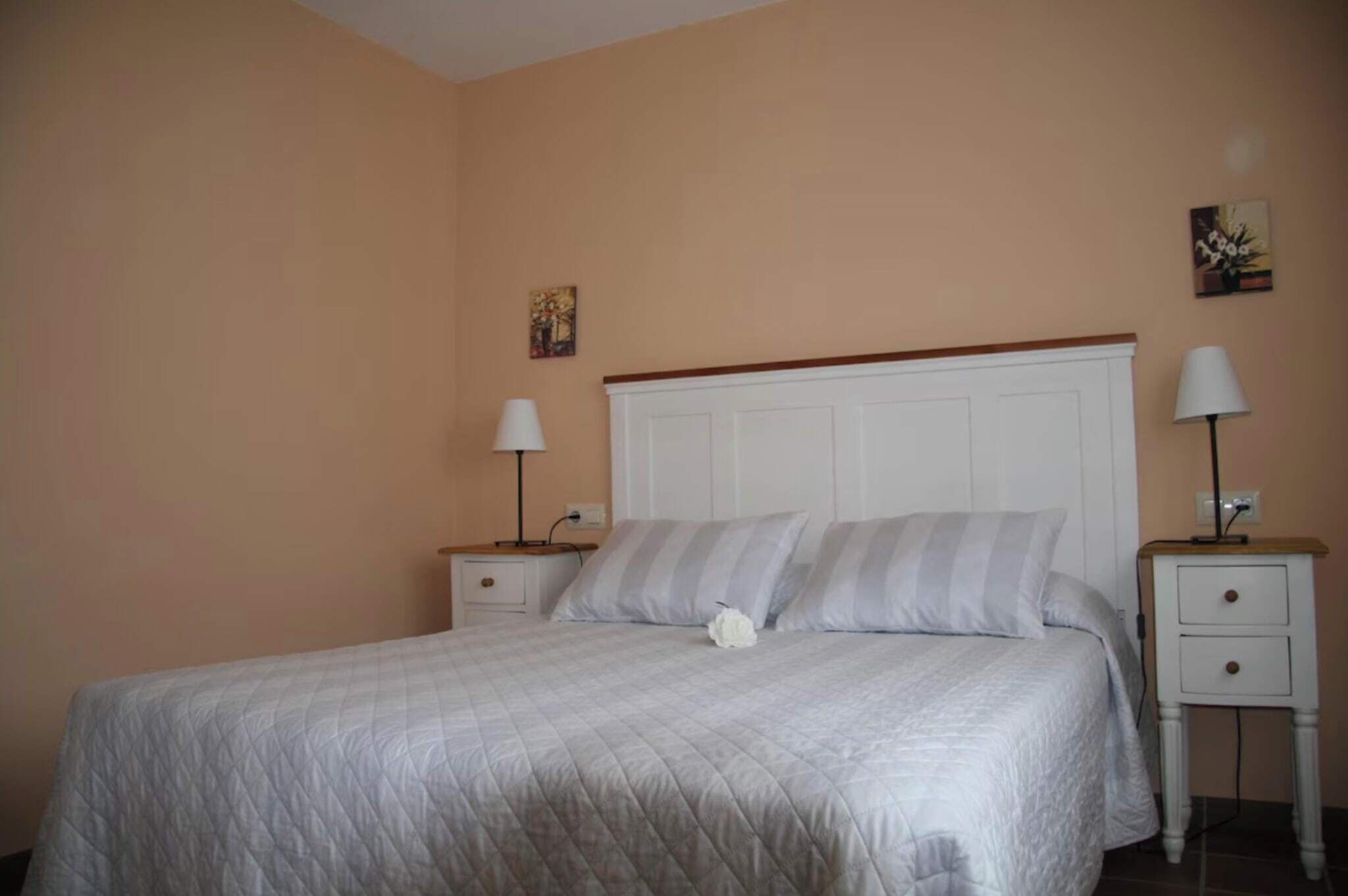 A neatly made bed with a white quilt, two bedside tables with lamps, and a small painting on the wall.