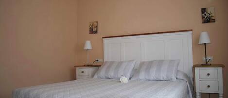 A neatly made bed with a white quilt, two bedside tables with lamps, and a small painting on the wall.