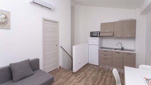 Cozinha compacta com micro-ondas, pia e armários, um sofá cinza e uma escada que leva a outro andar.