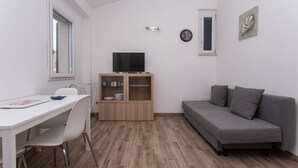 Um espaço compacto com mesa de jantar, sofá, televisão sobre um móvel de madeira e relógio de parede.