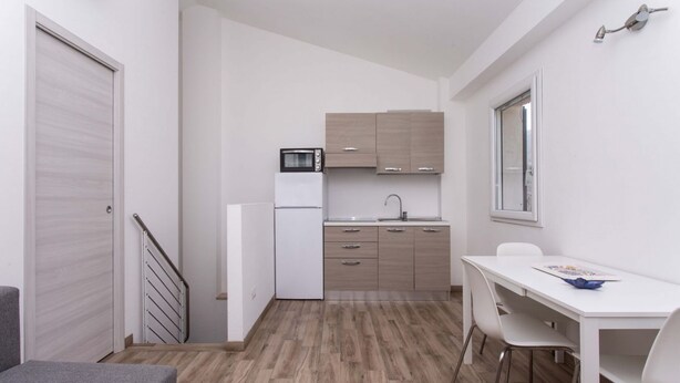 Cozinha compacta com micro-ondas, pia e armários, área de jantar com mesa e cadeiras, e escada que leva a outro cômodo.