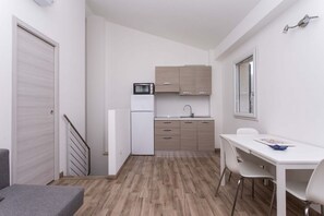 Ett kompakt kök med mikrovågsugn, diskho och skåp, en matplats med bord och stolar samt en trappa som leder till ett annat rum.