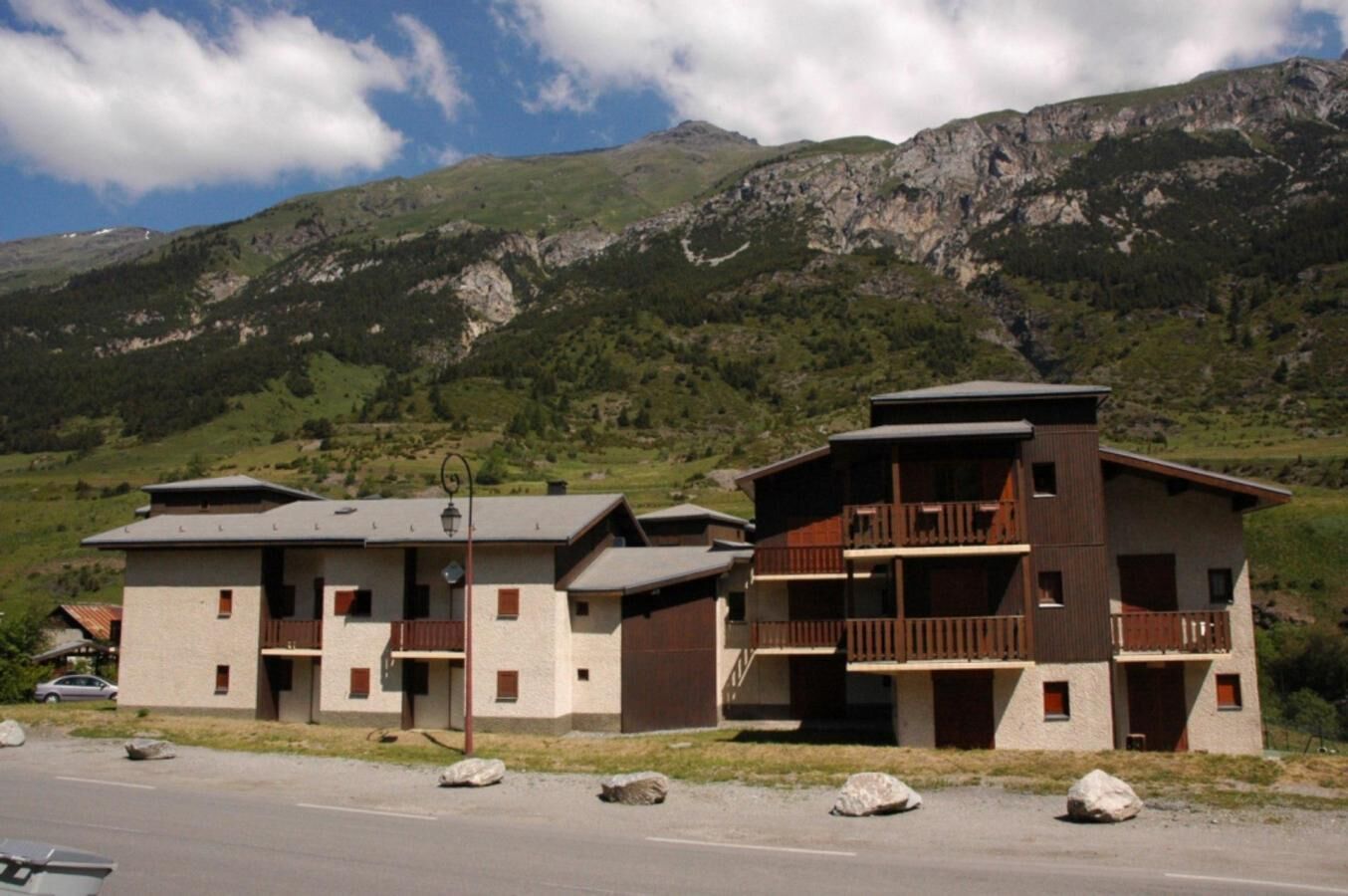 Ein zweistöckiges Gebäude mit einem Balkon, vor einer Berglandschaft.