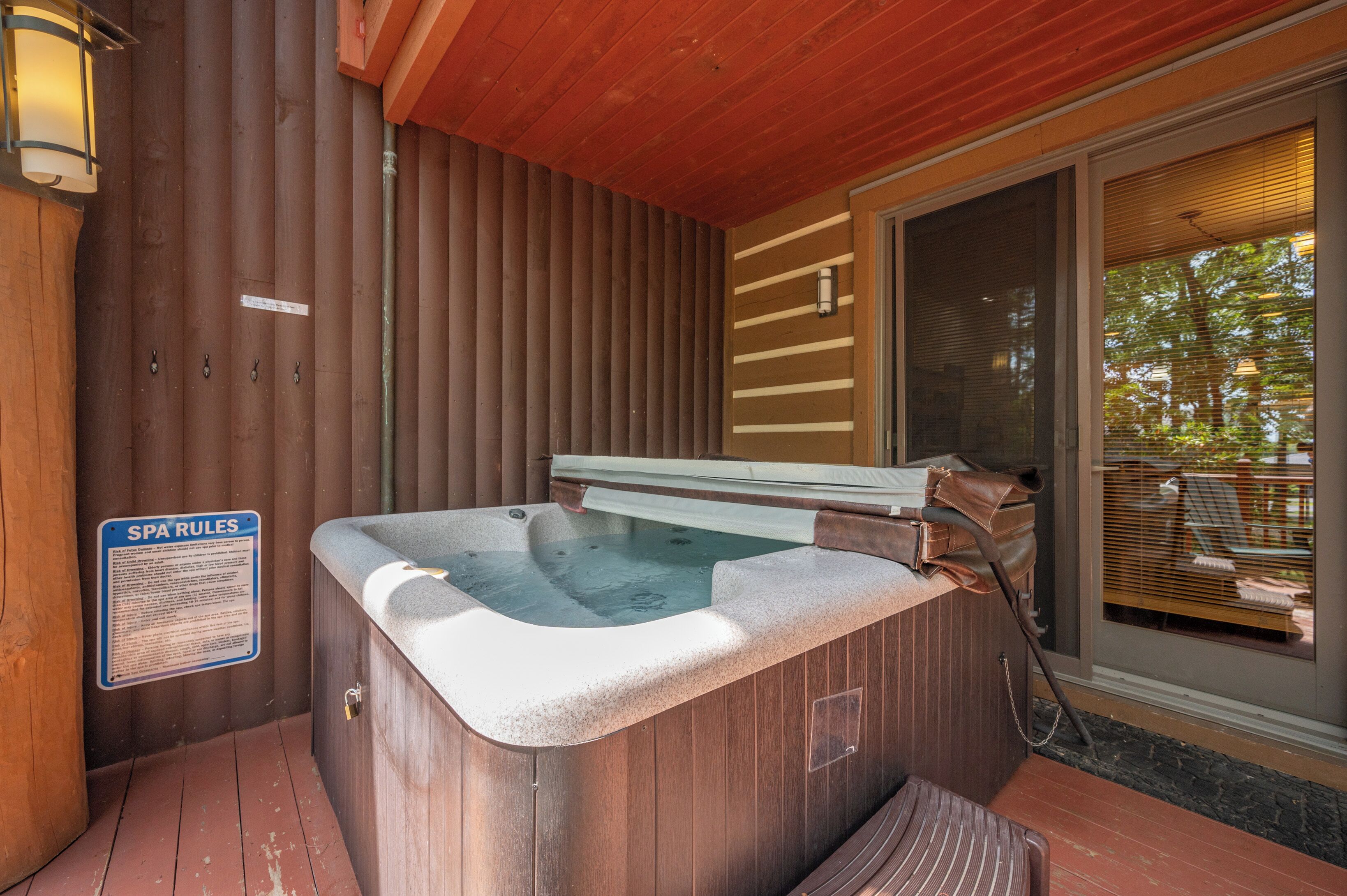 Un jacuzzi con cubierta de madera, un cartel con normas del spa y una puerta corrediza de vidrio que da a un espacio exterior.