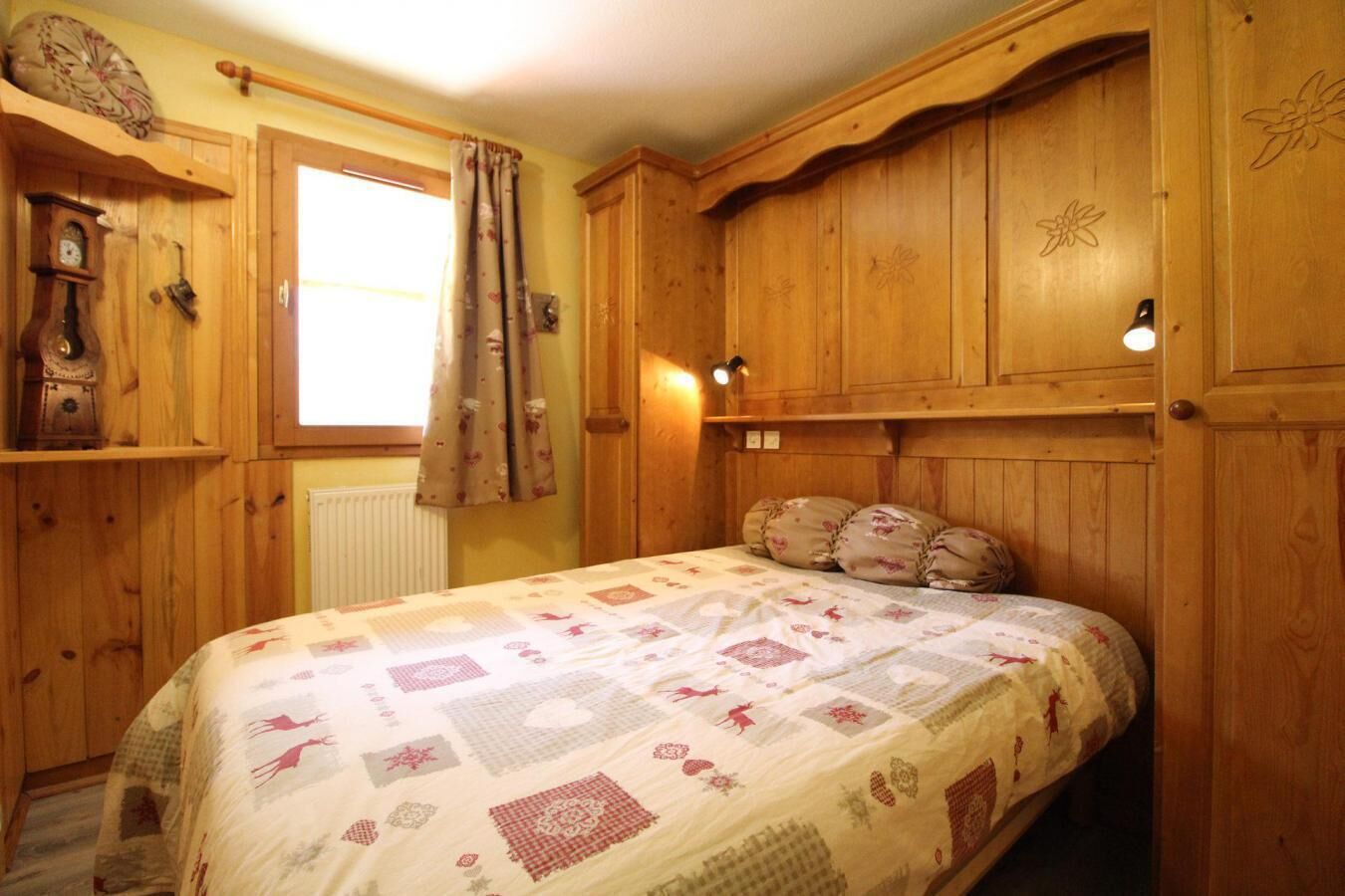 Ein Zimmer mit Holzboden, einem Bett, einem Fenster mit Vorhängen und Holzschränken.