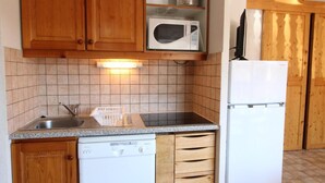 A compact kitchen with wooden cabinets, a microwave, a dishwasher, and a refrigerator. - 1st floor, balcony, tv, ski locker, 46m², Aussois (Aussois)