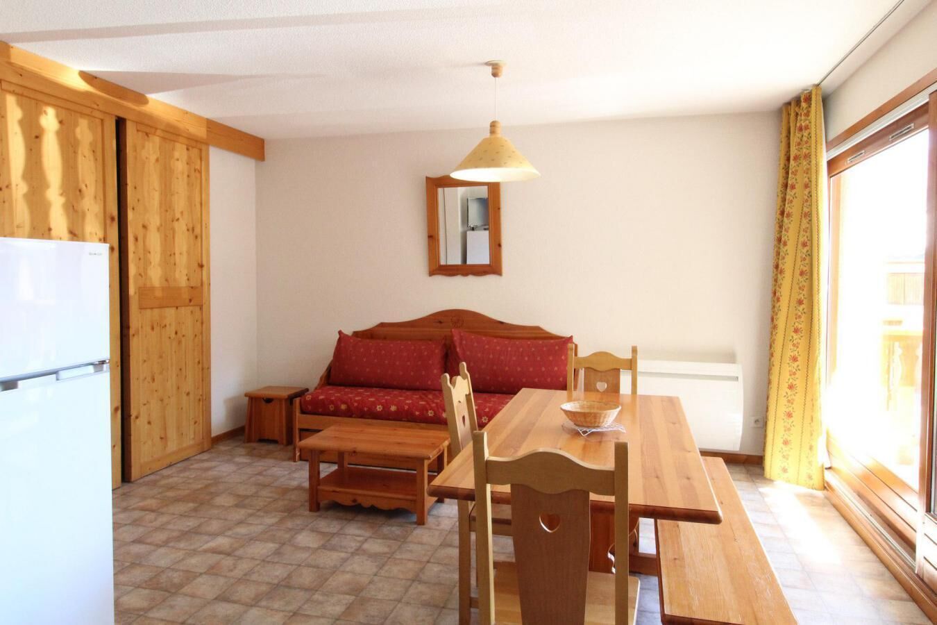 A compact kitchen with wooden furniture, a dining table, and a sofa.