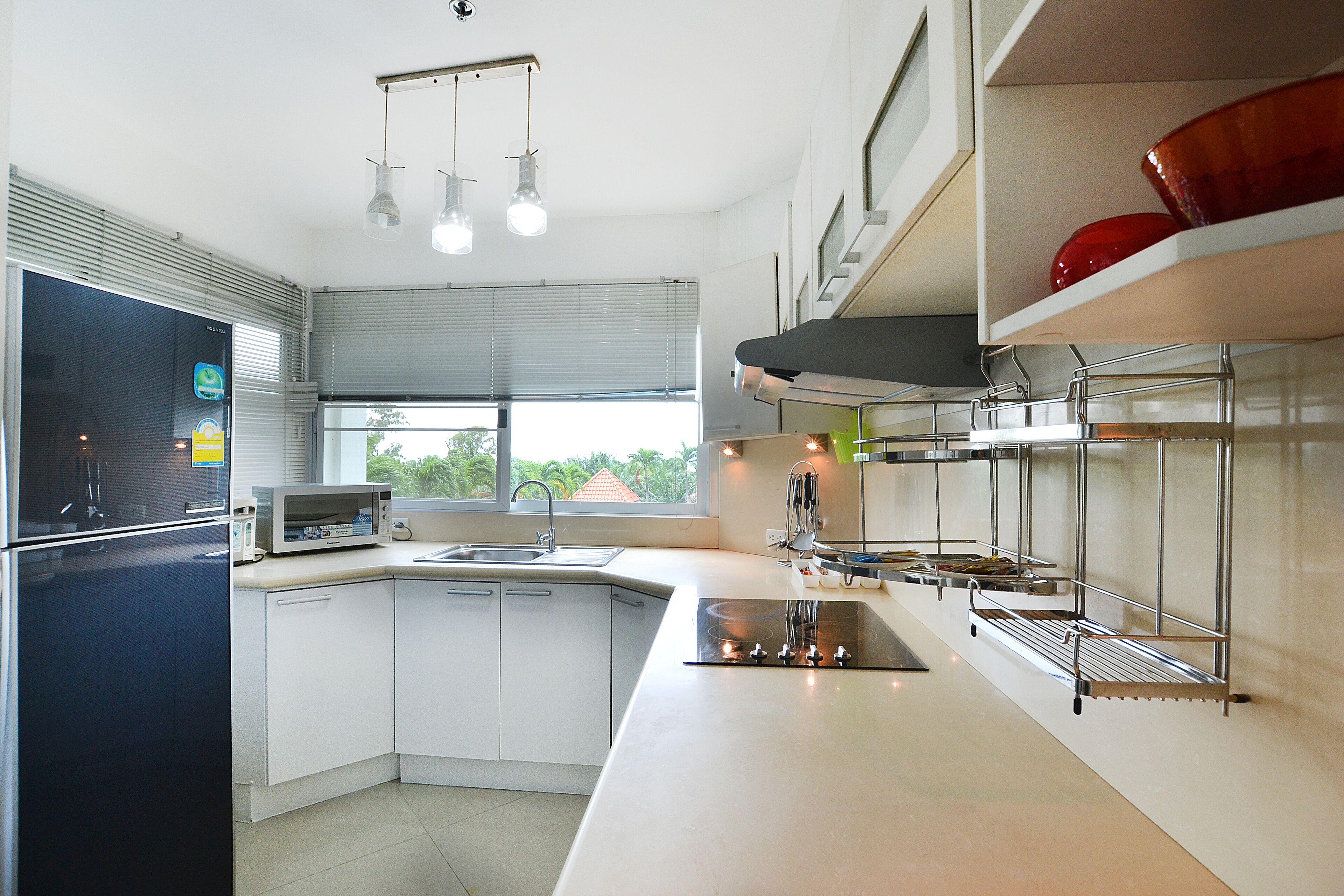 A modern kitchen with a black refrigerator, white cabinets, a microwave, and a sink. There are overhead lights and a window with blinds.