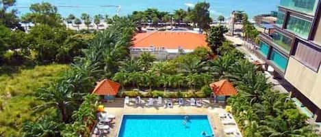 A hotel pool with a view of the ocean and boats, surrounded by palm trees and lounge chairs.