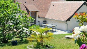 A house with a tiled roof, a small patio with a table and chairs, and a garden with various plants and flowers. - Typical barn from the 17th century, 120 square meters of living space (La Membrolle-sur-Choisille)