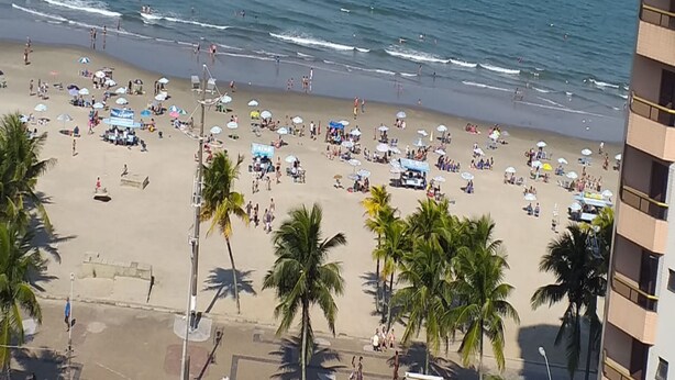 Ein Strand mit Palmen, Sonnenschirmen und Menschen.