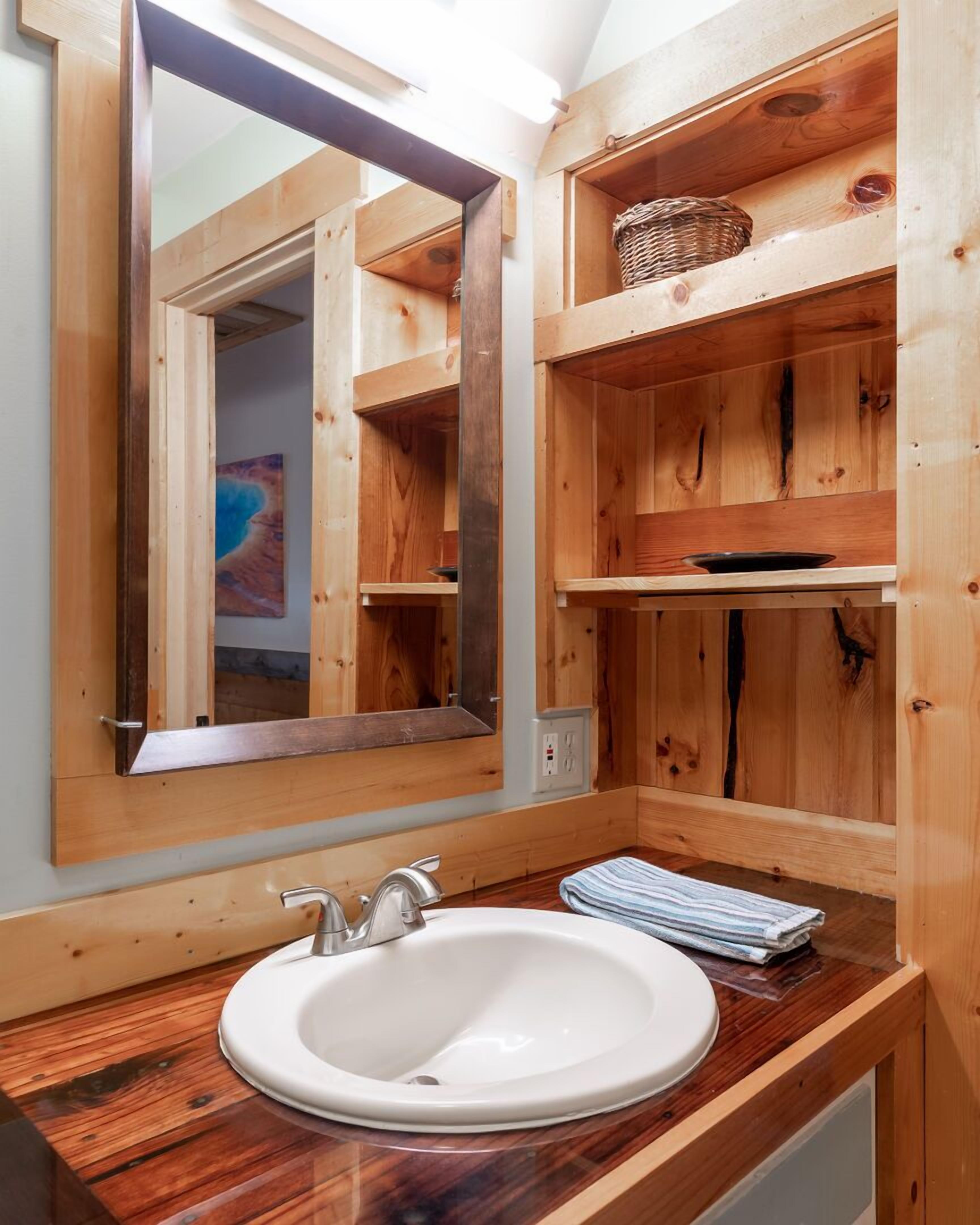 Een houten badkamer met een grote spiegel, een wit wastafelmeubel en houten planken.