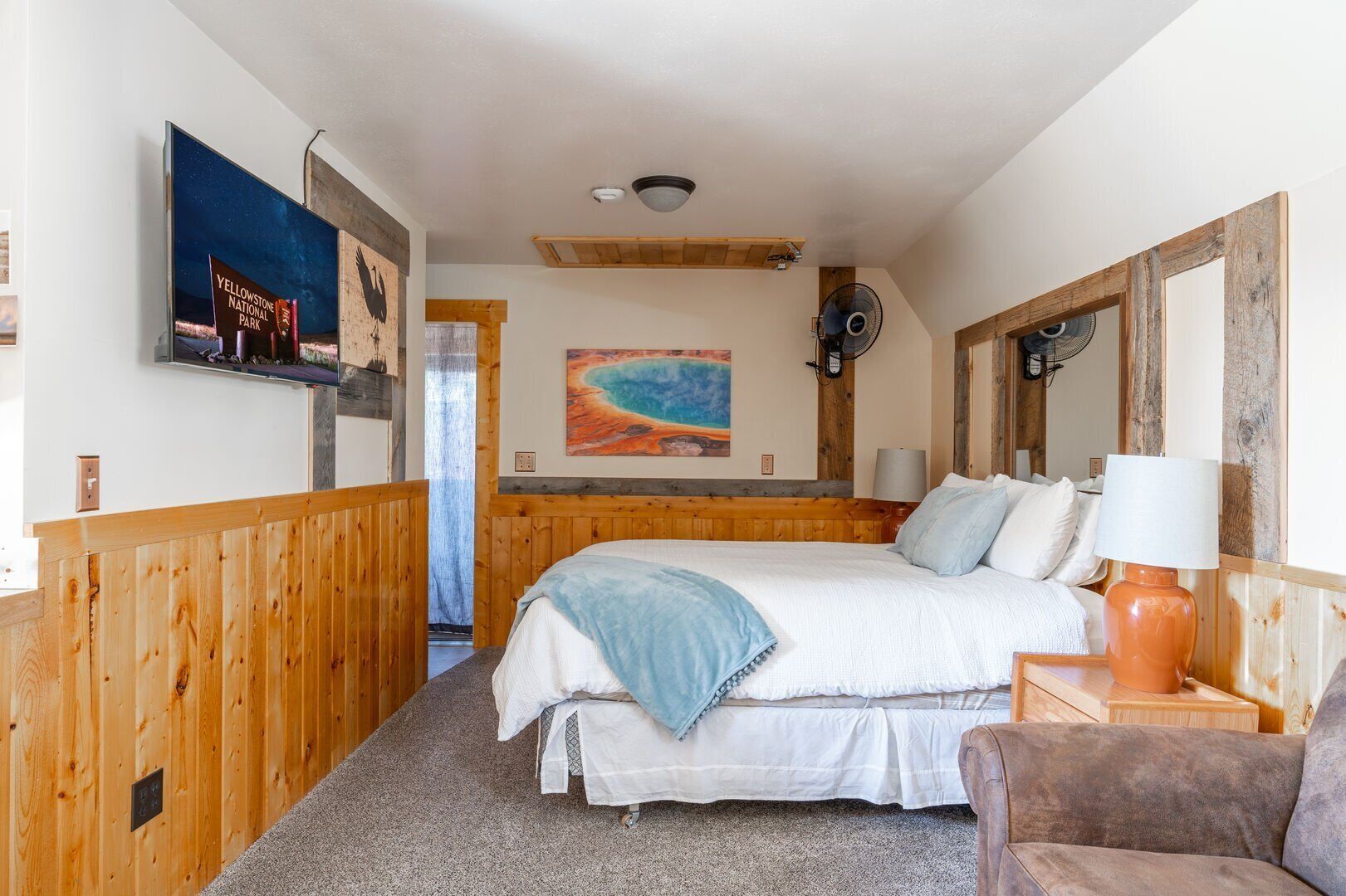 Ein Schlafzimmer mit einem hölzernen Kopfteil, einem Bett mit weißer Bettwäsche, einer blauen Tagesdecke, einem Nachttisch aus Holz mit einer Lampe und einem Gemälde mit einer Strandansicht.