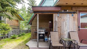 Une cuisine extérieure en bois, équipée d’un barbecue, de deux chaises et d’une bouteille de gaz.