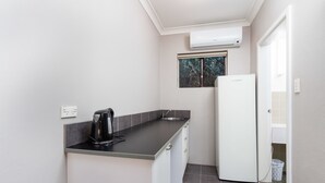 A compact kitchen with a black countertop, a white refrigerator, and a window with a view of trees. - Archibald Hotel (Kurrajong Heights)