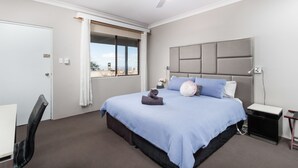 A bedroom with a bed, a desk, a chair, a window with curtains, and a ceiling fan. - Archibald Hotel (Kurrajong Heights)