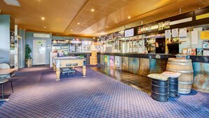 A bar area with a pool table, stools, and a bar counter with various items and posters. - Archibald Hotel (Kurrajong Heights)